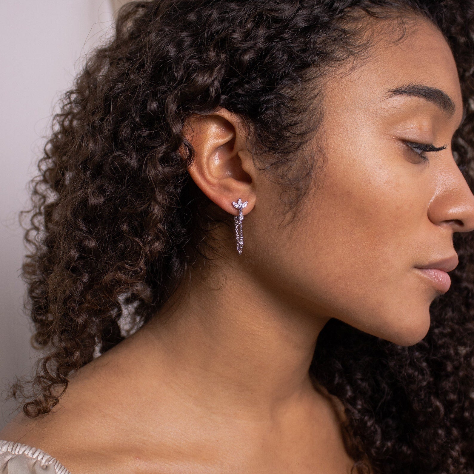Woman with curly hair wearing Genesis Chain Earrings, shown in profile against a neutral background.