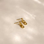 The Amia Pave Link Earrings, featuring small pavé accents, are displayed on a soft beige surface under gentle lighting.