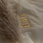 Five Nella Name Necklaces on cream fabric beside pampas grass, each custom nameplate displays Shelby, Nicholas, Emily, Priscilla, Angela, and Malaka—a stunning display of personalized jewelry.