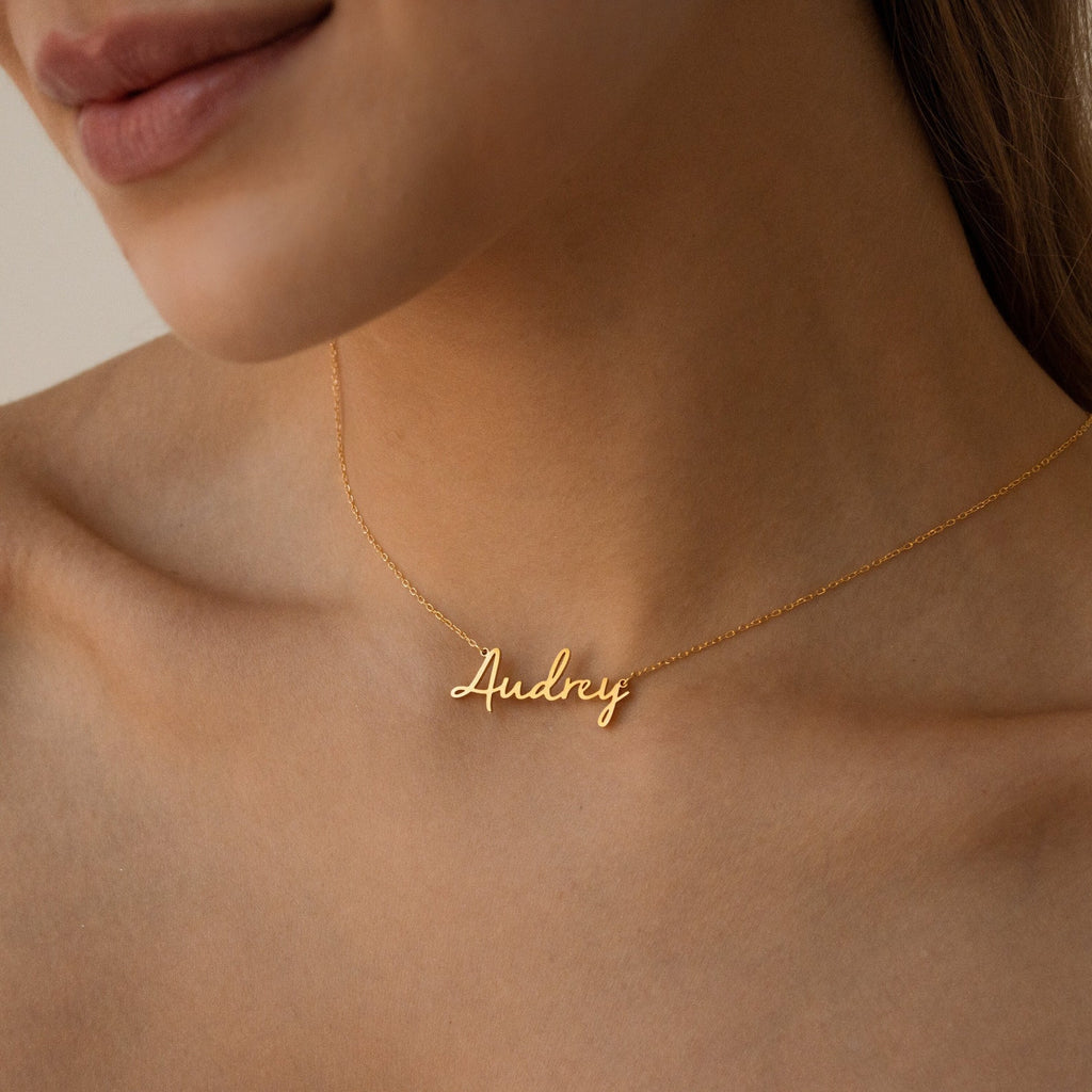 Close-up of a woman wearing the Nella Name Necklace, featuring the name Audrey in elegant cursive letters.