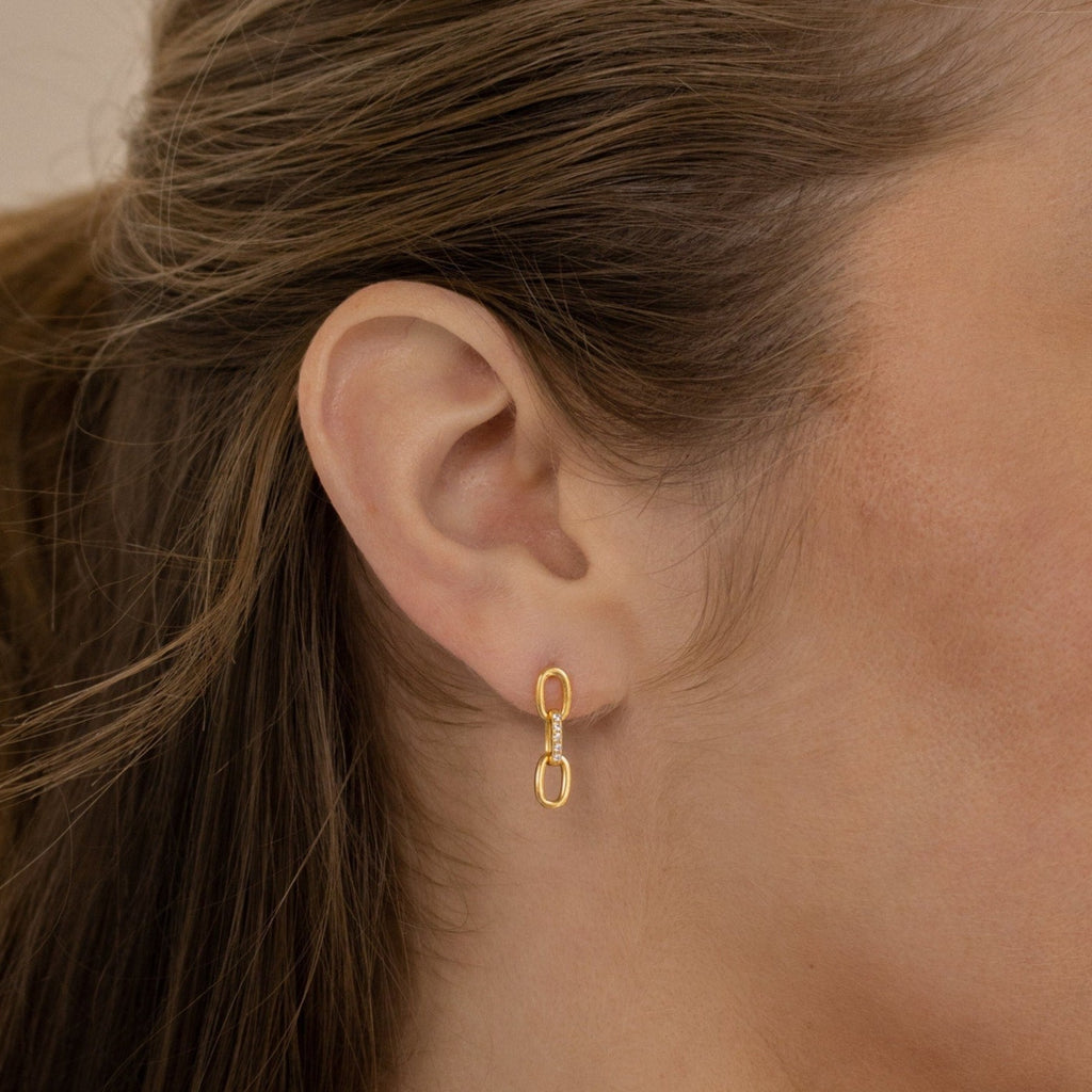 Close-up of a woman's ear adorned with the Amia Pave Link Earrings, showcasing a gold double oval paperclip chain design and subtle pavé accents.