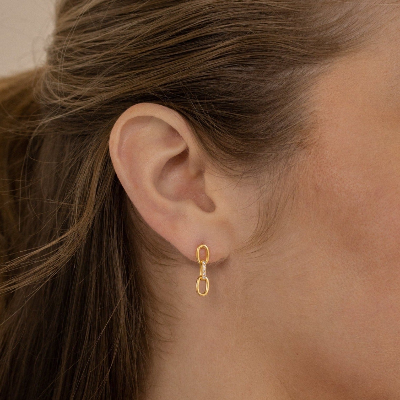 Close-up of a woman's ear adorned with the Amia Pave Link Earrings, showcasing a gold double oval paperclip chain design and subtle pavé accents.
