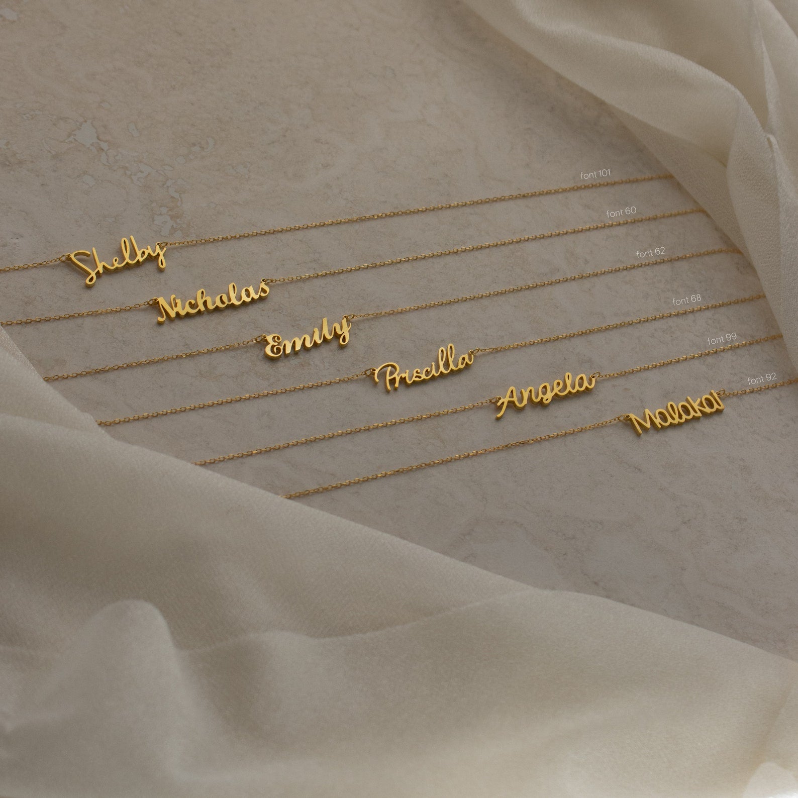 Six Grace Name Necklaces displayed on a beige fabric background, each featuring names in elegant cursive script. Perfect as custom nameplate jewelry for a unique, personal touch.