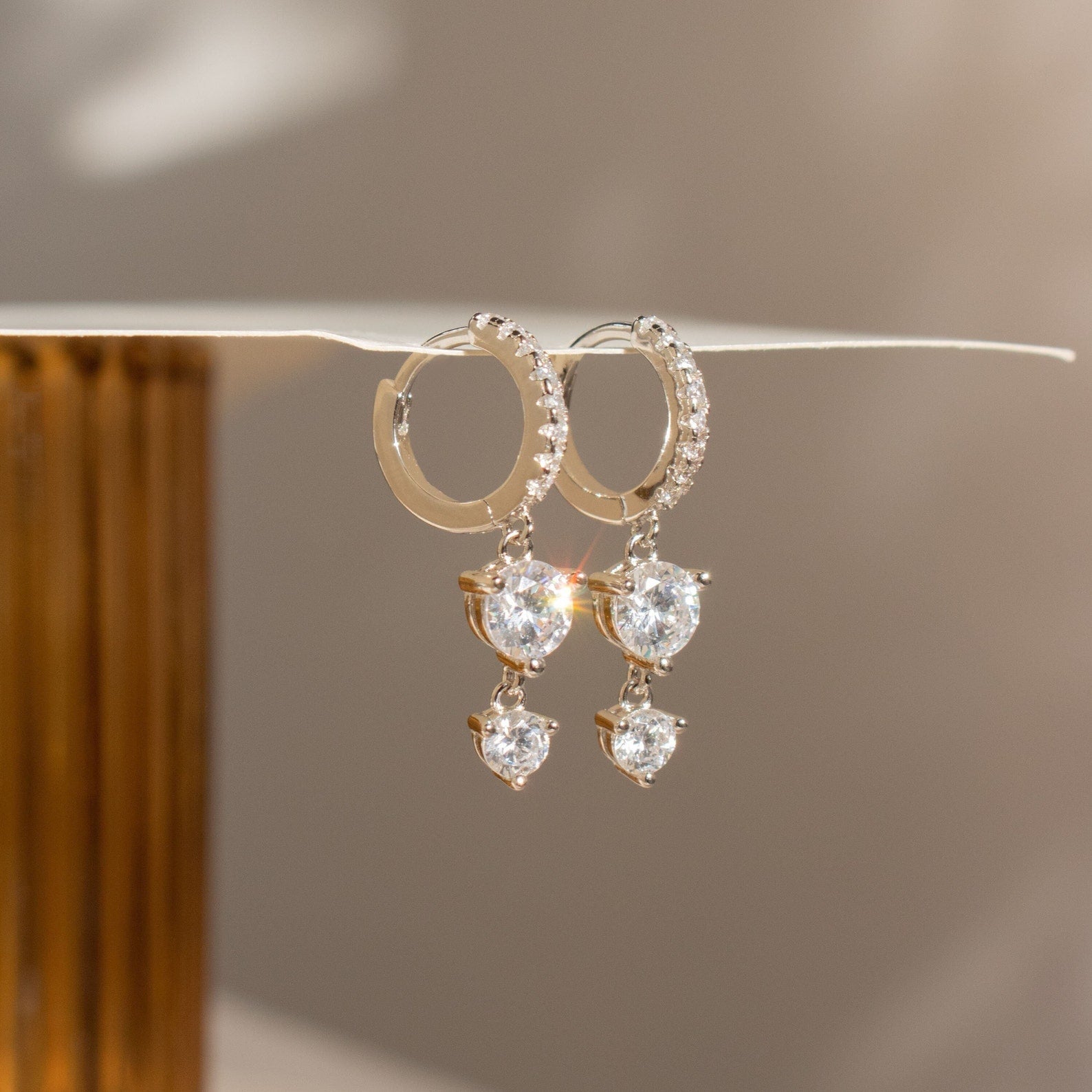 Caroline Pave Drop Huggies feature gold hoops adorned with teardrop-shaped crystals that sparkle in natural light, adding a touch of elegance to any look.