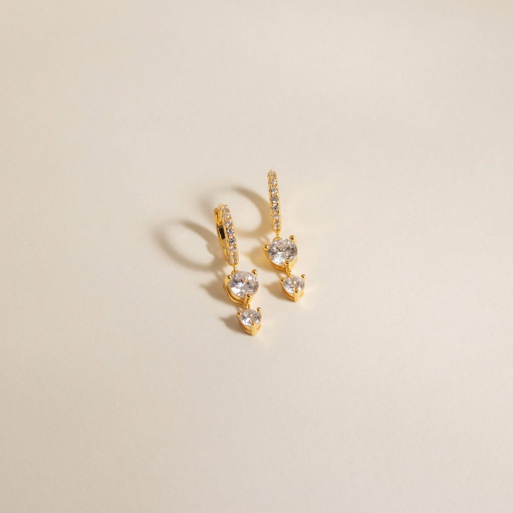 Caroline Pave Drop Huggies: Gold hoops featuring small diamonds and two larger stones on each, shown against a plain light background.
