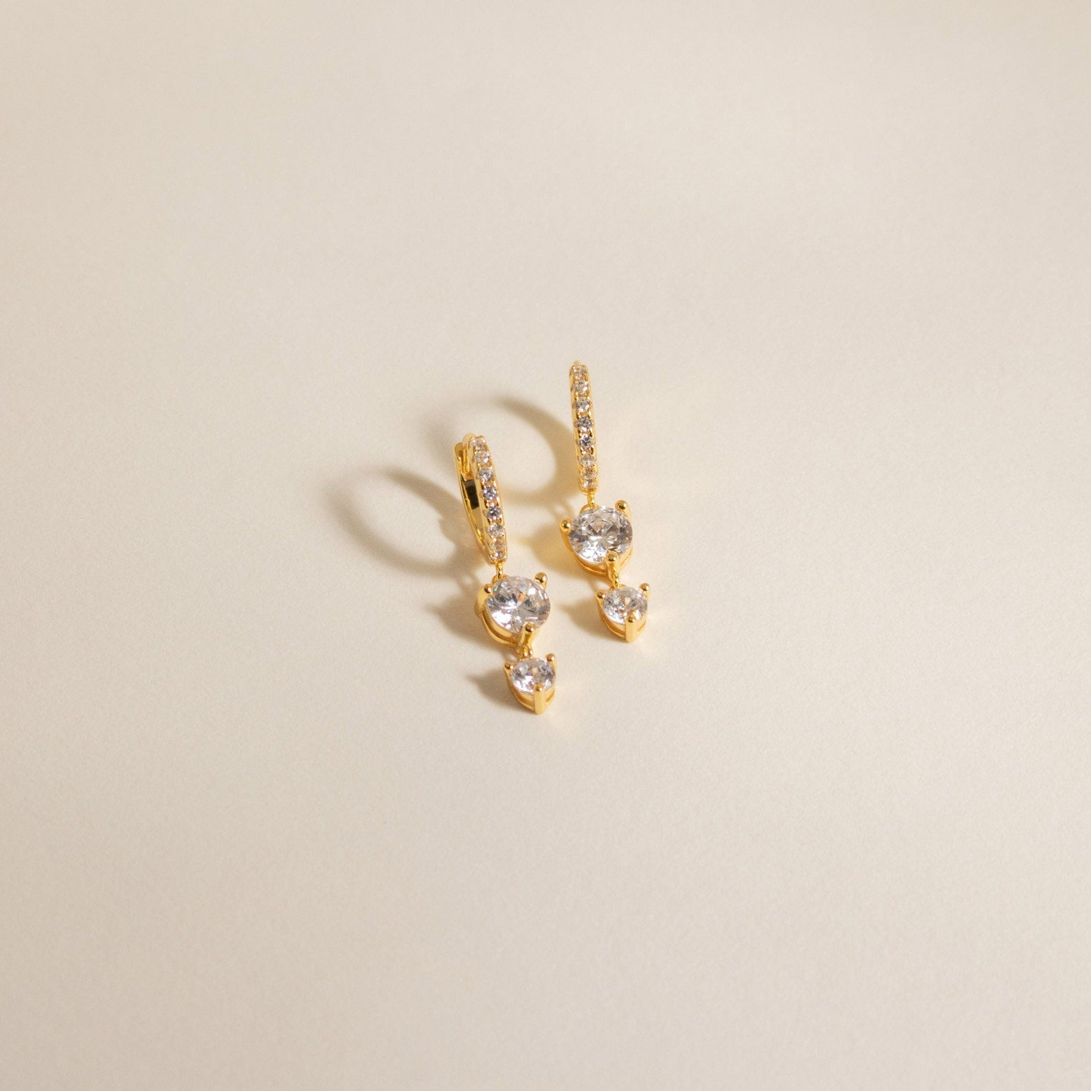 Caroline Pave Drop Huggies: Gold hoops featuring small diamonds and two larger stones on each, shown against a plain light background.