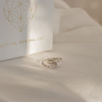 Two Aster Pave Twisted Hoops in silver sit on cream fabric next to a white box labeled AITLYN MINIMALIST—ideal for anyone who loves dainty earrings.