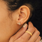Close-up of Glacier Diamond Studs on a person's ear, complemented by gold rings on their hand—an elegant pairing that looks stunning with asymmetrical earrings for a modern style.