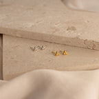 The Trio Sphere Studs in silver and gold are shown on beige stone surfaces with a soft background—ideal for an elegant earring stack or alternative piercings.