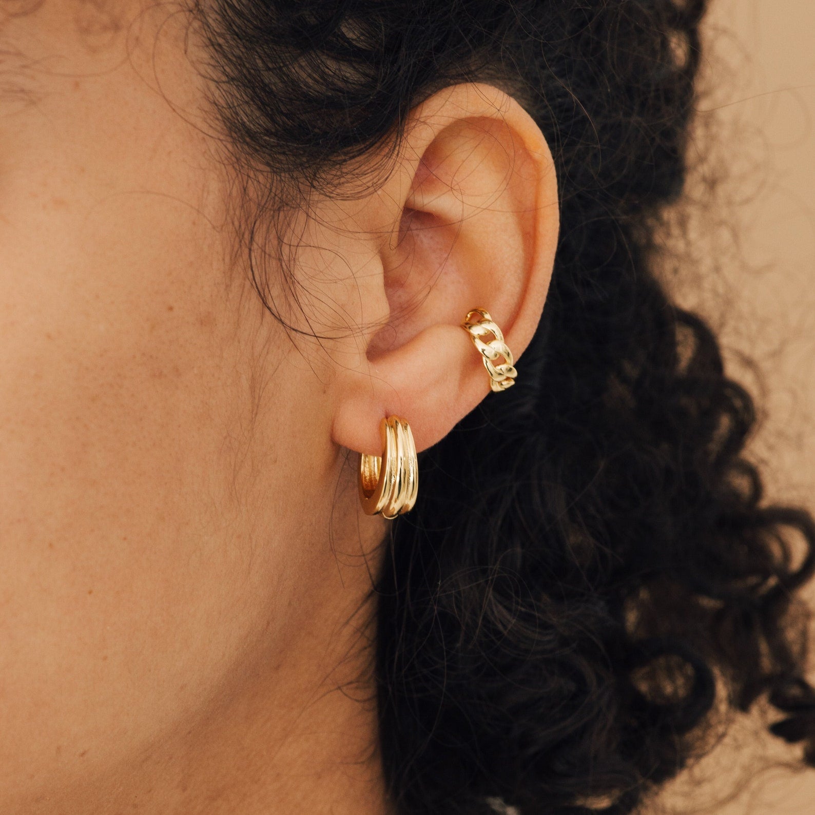 Close-up of an ear with curly hair, wearing Canal Chunky Hoops as everyday earrings and a gold ear cuff.