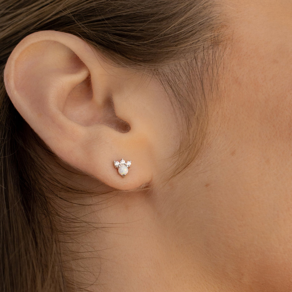 Close-up of a woman's ear wearing Jackie Opal Studs—dainty earrings with a round opal gem and three smaller stones above.
