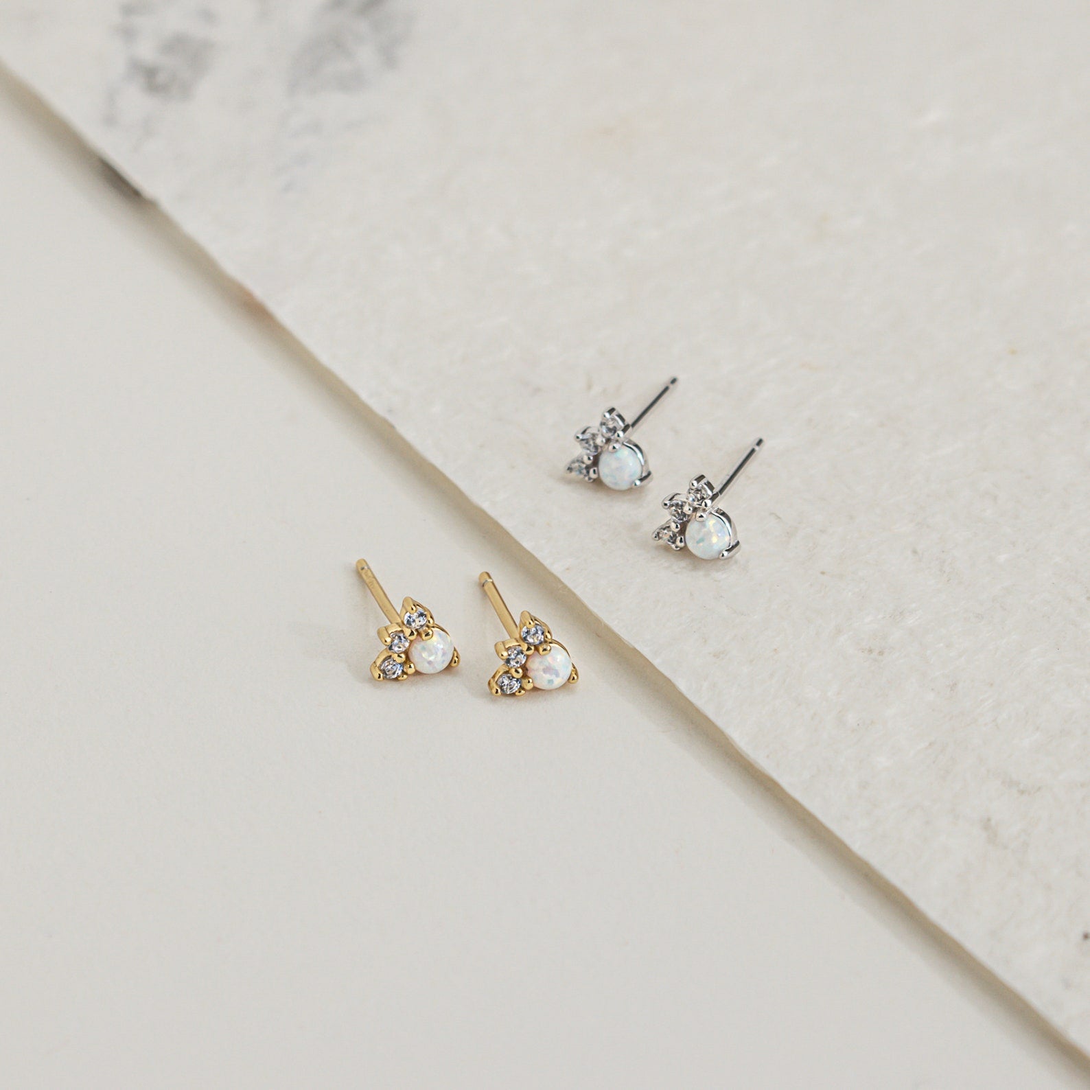 The Dainty Opal Earrings Set includes two pairs of elegant earrings—one gold and one silver—with pearl and crystal accents, beautifully displayed on a light textured surface.