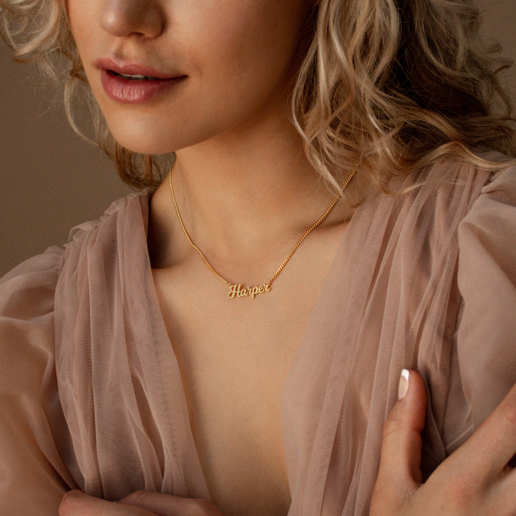 A woman wears the Mellow Name Necklace in Curb Chain, showcasing her personalized jewelry—a timeless piece that adds a unique touch to her style.