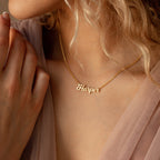 A woman wears a Mellow Name Necklace in Curb Chain—a gold, personalized piece featuring the name Harper elegantly crafted in cursive letters.