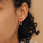 Close-up of a person's ear with curly hair, wearing Indiana Beaded Hoops—small gold hoop earrings accented with chic tiny beads.