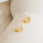 Maze Half Hoops—gold wavy earrings inspired by our Maze Huggies collection—are shown on a light, curved surface. They’re perfect for adding a unique touch to your earring stack.