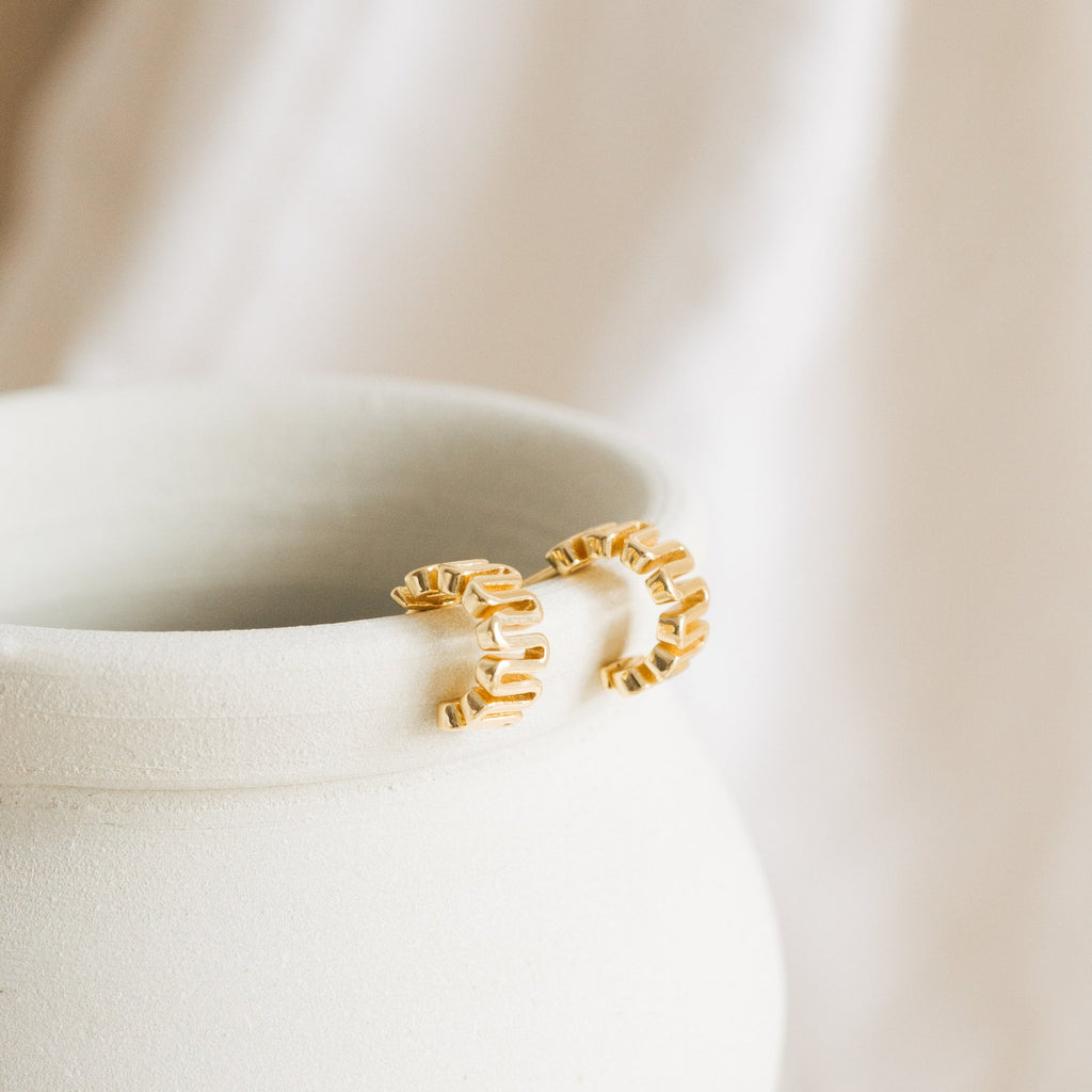 Maze Half Hoops, featuring a chunky textured design, rest on a matte white ceramic vase—perfect for a unique earring stack or paired with our Maze Huggies.
