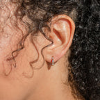 A close-up of a person's ear with curly hair wearing Kenia Diamond Huggies—elegant, small silver hoop earrings that shimmer with timeless sparkle.