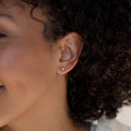 Close-up of a person with curly hair wearing Trio Sphere Studs—small, silver flower-shaped earrings ideal for an elegant earring stack or styling with other piercings.
