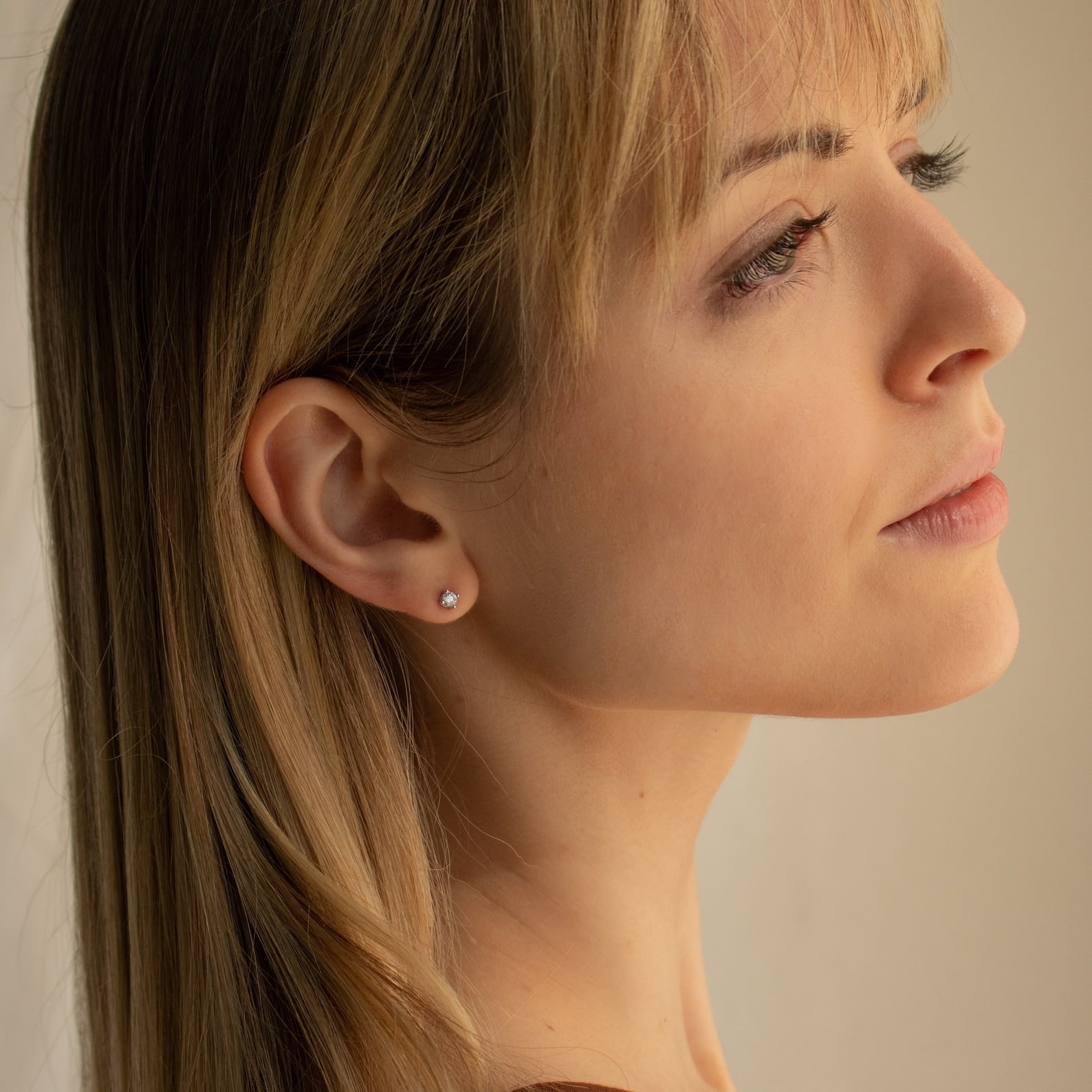 A blonde woman in profile looks thoughtful against a neutral background, wearing the Booker Classic Diamond Studs.