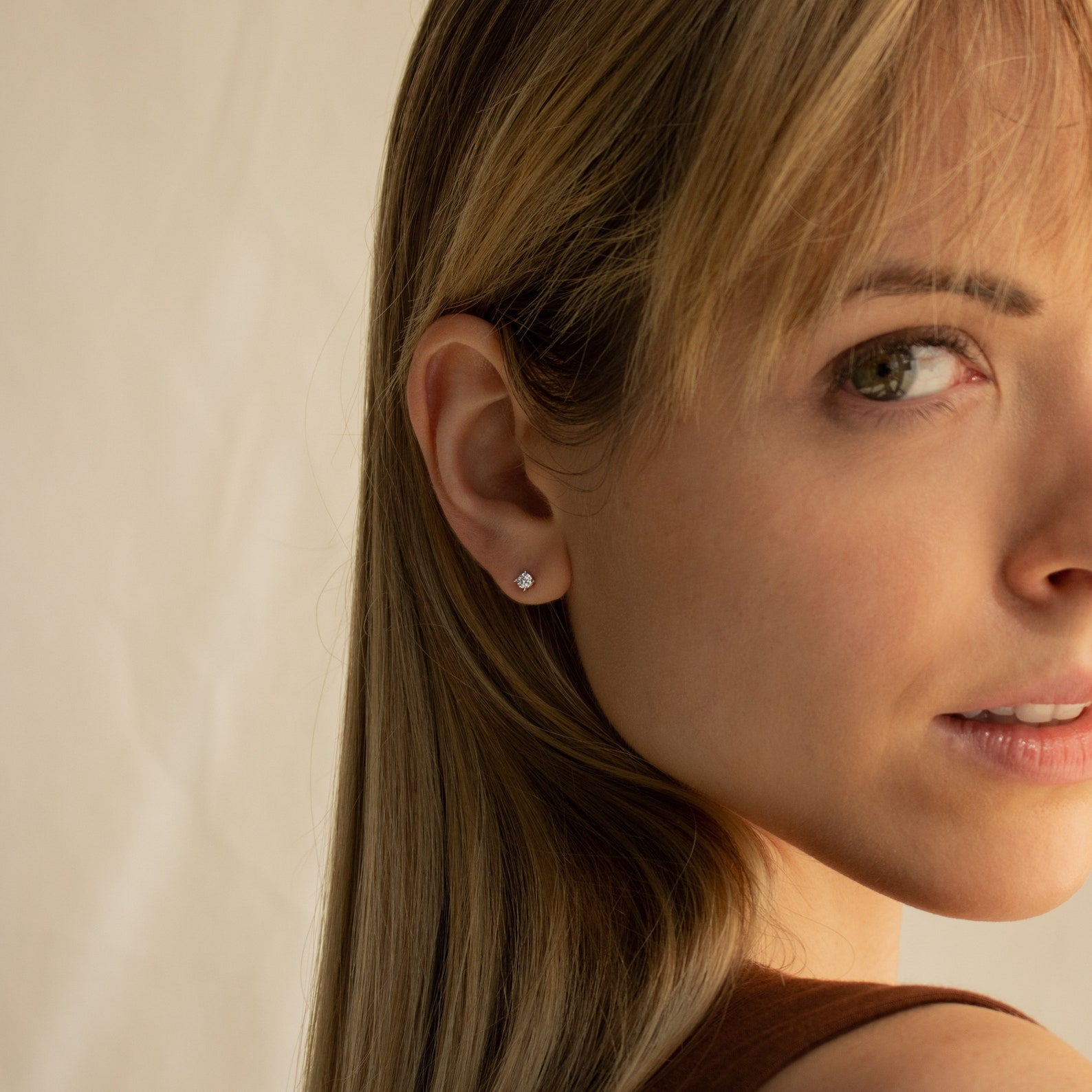 Close-up of a woman with blonde hair wearing Booker Classic Diamond Studs, looking toward the camera.