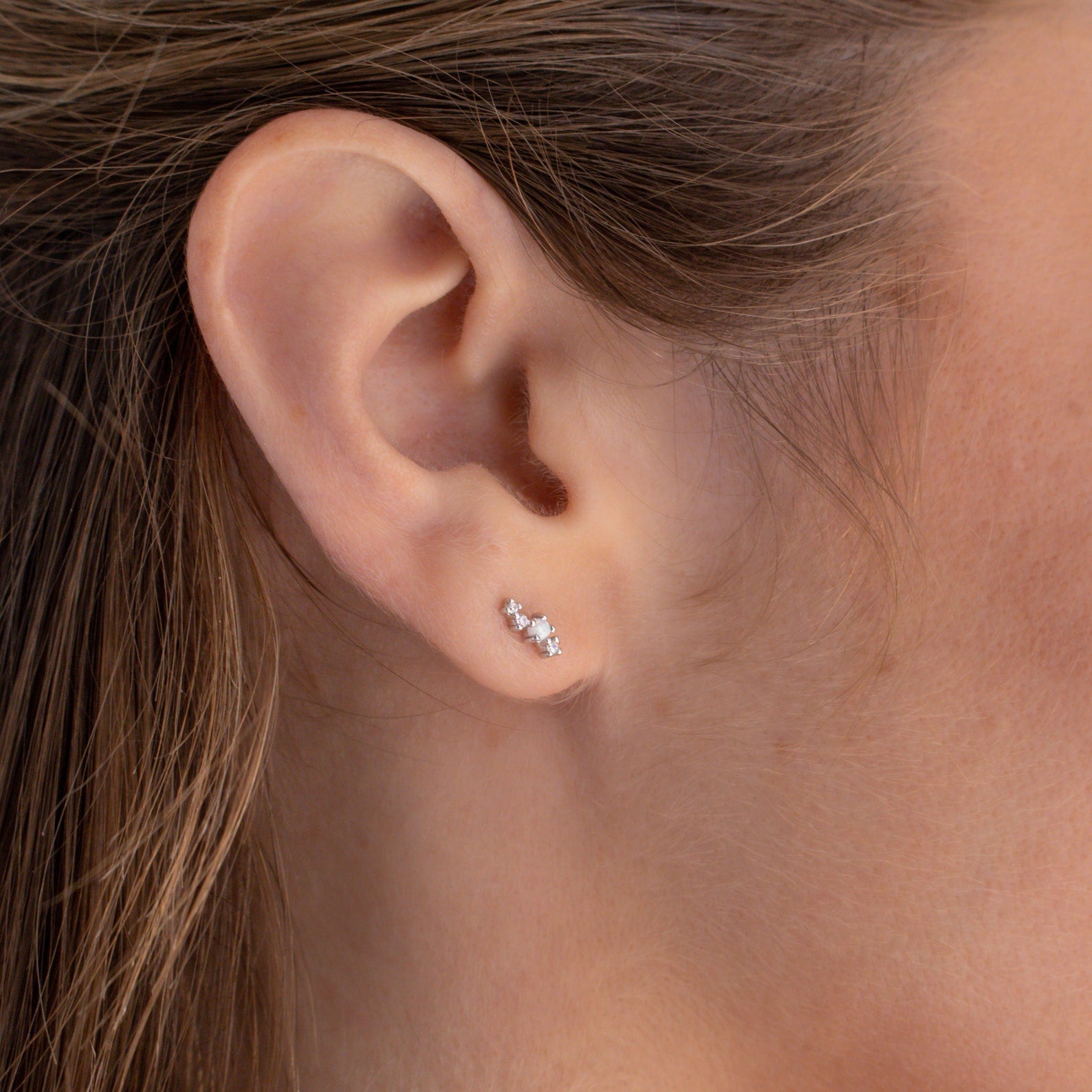 Close-up of a woman's ear wearing Nile Opal and Diamond Studs—a delicate, three-stone design inspired by constellations.