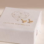 Two Nile Opal and Diamond Studs, inspired by constellations, are displayed on a white textured jewelry box labeled Caitlyn Minimalist.