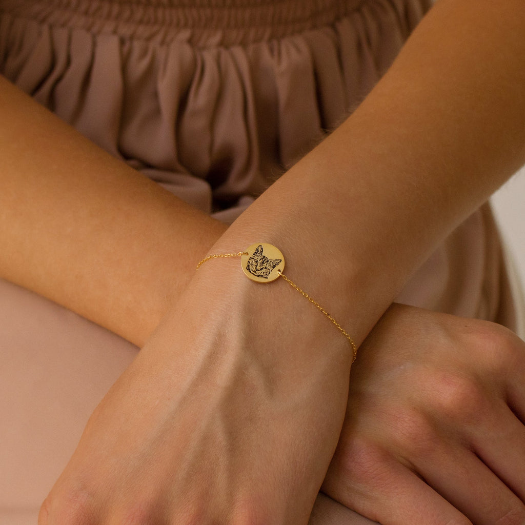 The Pet Portrait Disc Bracelet features a round gold charm engraved with a cat, worn on the wrist against a beige outfit—a beautiful piece of pet jewelry and a thoughtful memorial gift for animal lovers.
