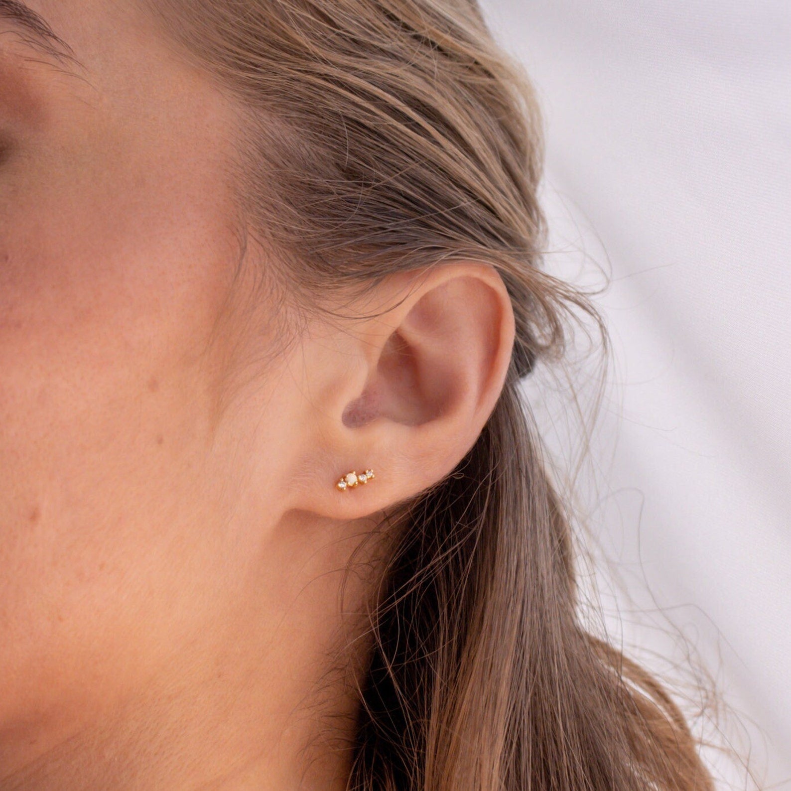 Close-up of a woman’s ear with Nile Opal and Diamond Studs—constellation-inspired earrings—her hair tucked behind her ear.