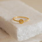 The Eden Sun Ring features a delicate boho-chic sunburst design with textured gold and a small central stone, displayed on a marble surface.