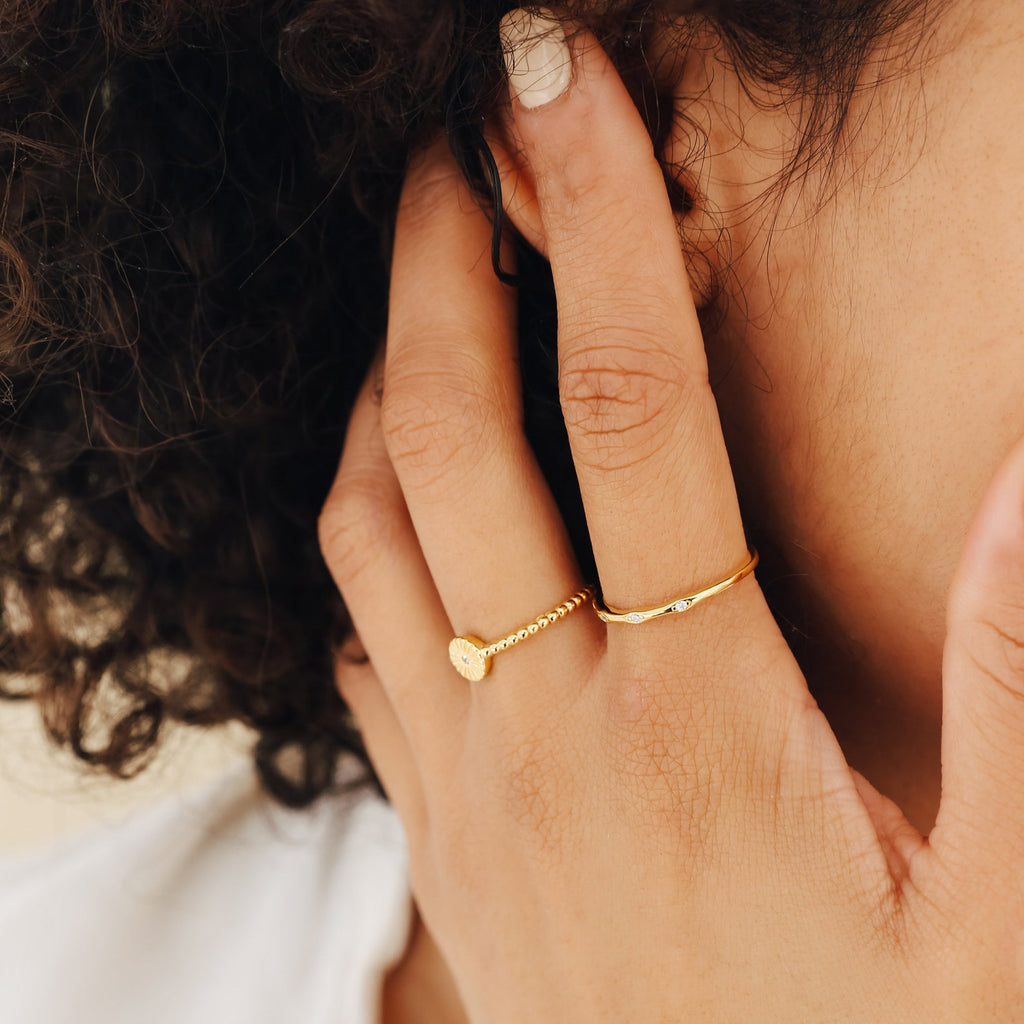 A hand wearing the Eden Sun Ring touches curly hair near the ear, nails painted in a light shade.