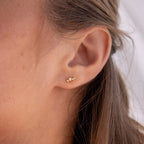 Close-up of a woman's ear wearing Nile Opal and Diamond Studs—small gold floral earrings with constellation-inspired design; her light brown hair is tucked behind her ear.