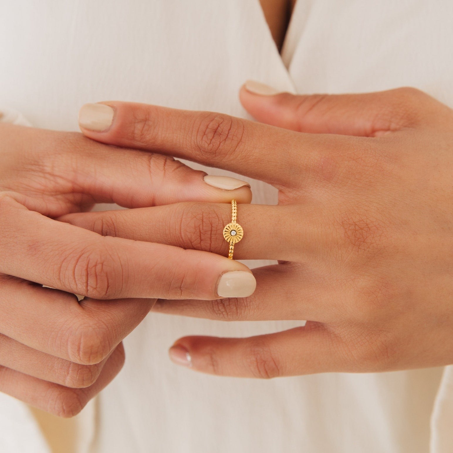 A person wears the Eden Sun Ring on their finger, paired with a cream-colored top for a subtle boho-chic style.