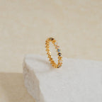 The Rainbow Crystal Ring, featuring pastel-toned gemstones set in delicate gold, rests on a textured white stone surface.