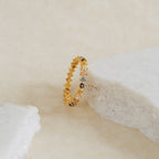 The Rainbow Crystal Ring, a vintage-inspired band with pastel gemstones, shines against a white stone on a beige surface.