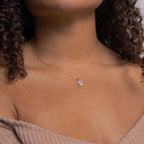 Gold necklace with a marquise-cut crystal pendant worn by a model in a taupe ribbed off-the-shoulder top, showcasing the stone's clarity and brilliance against warm skin tones.
