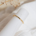 The Juliet Diamond Ring, featuring delicate diamonds, is displayed on rolled white paper against a soft, neutral background.