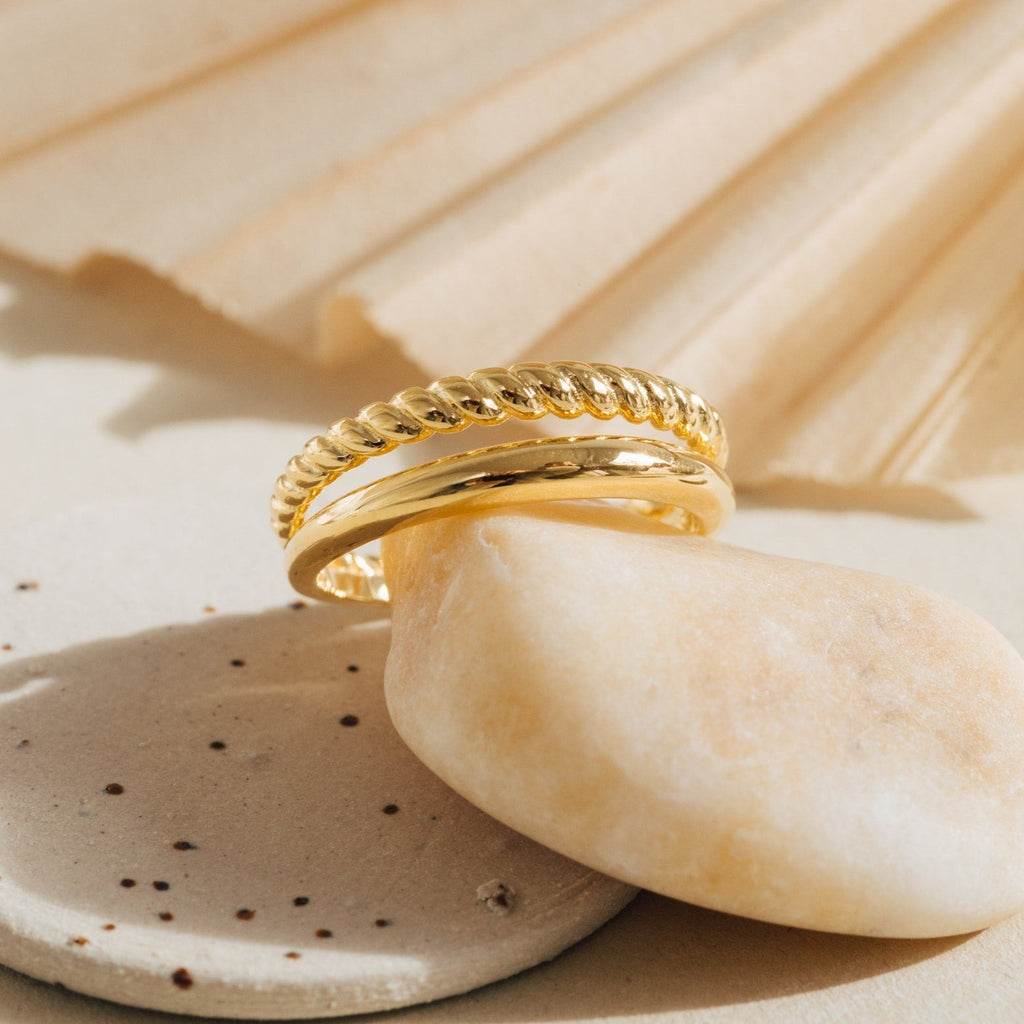 Close-up of Chelsea Duo Ring in gold with one twisted rope band and one polished smooth band, styled on neutral stone accents.