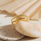 Close-up of Chelsea Duo Ring in gold with one twisted rope band and one polished smooth band, styled on neutral stone accents.