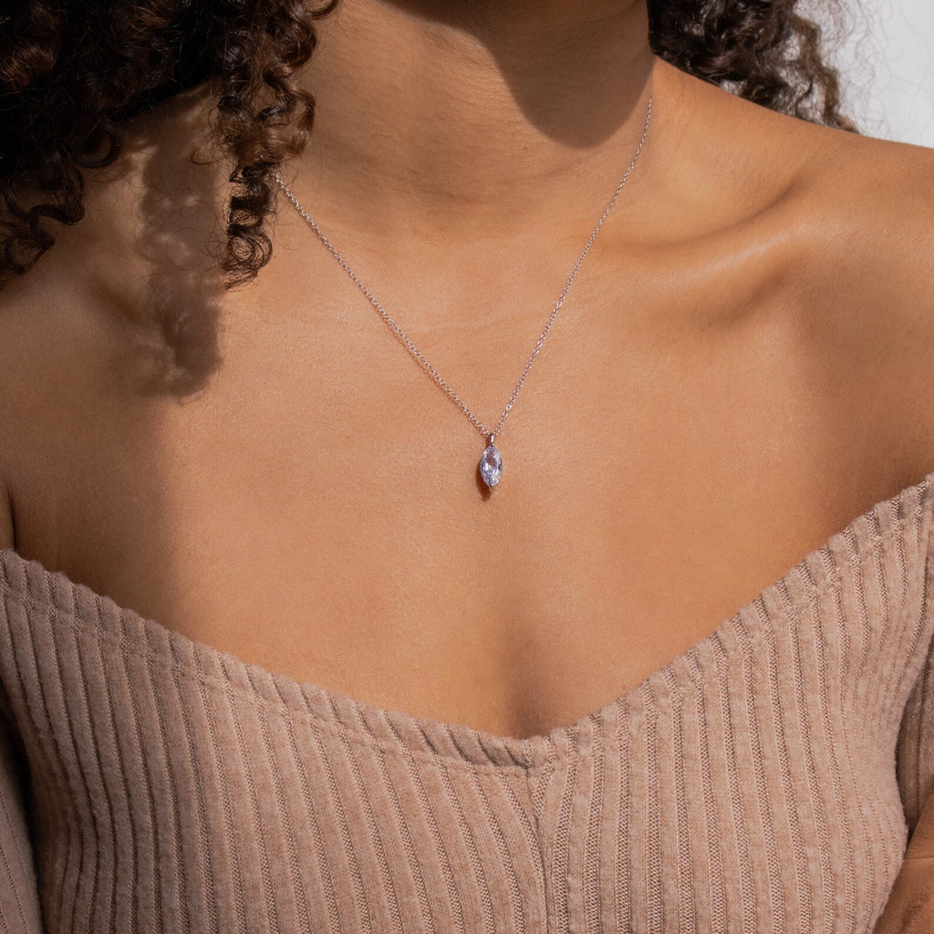 A woman wears the Athens Diamond Necklace—a delicate silver teardrop pendant on a fine cable chain—styled with an off-shoulder ribbed beige top.