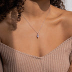 A woman wears the Athens Diamond Necklace—a delicate silver teardrop pendant on a fine cable chain—styled with an off-shoulder ribbed beige top.
