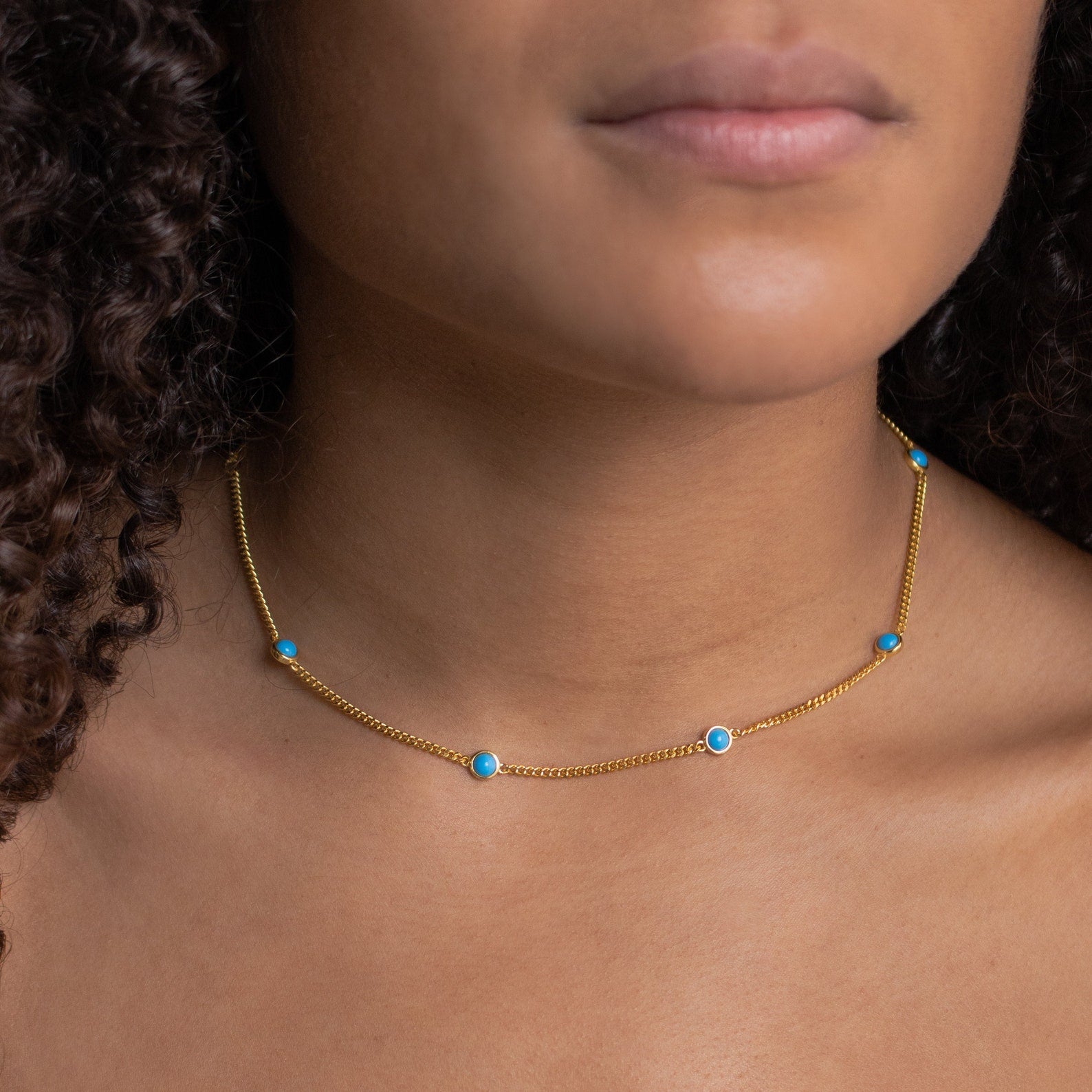 A woman wears the Santorini Turquoise Choker, a gold necklace with evenly spaced small turquoise drops around her neck.