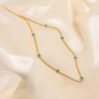 The Santorini Turquoise Choker features a gold chain with evenly spaced turquoise drops, beautifully showcased on smooth cream-colored satin.