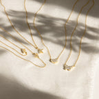 The Pave Initial Necklace, a delicate gold piece with a sparkling pendant, is displayed on light textured fabric—perfect for fans of personalized jewelry.
