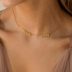 The Preppy Multiple Name Necklace in Curb Chain, featuring names in a youthful font, rests on a woman's neck styled with a beige sheer top and finished with a dainty curb chain.