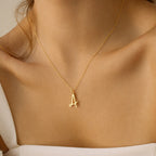 A woman wears the Nella Letter Necklace, featuring a gold pendant shaped like the letter A that elegantly rests on her neck.