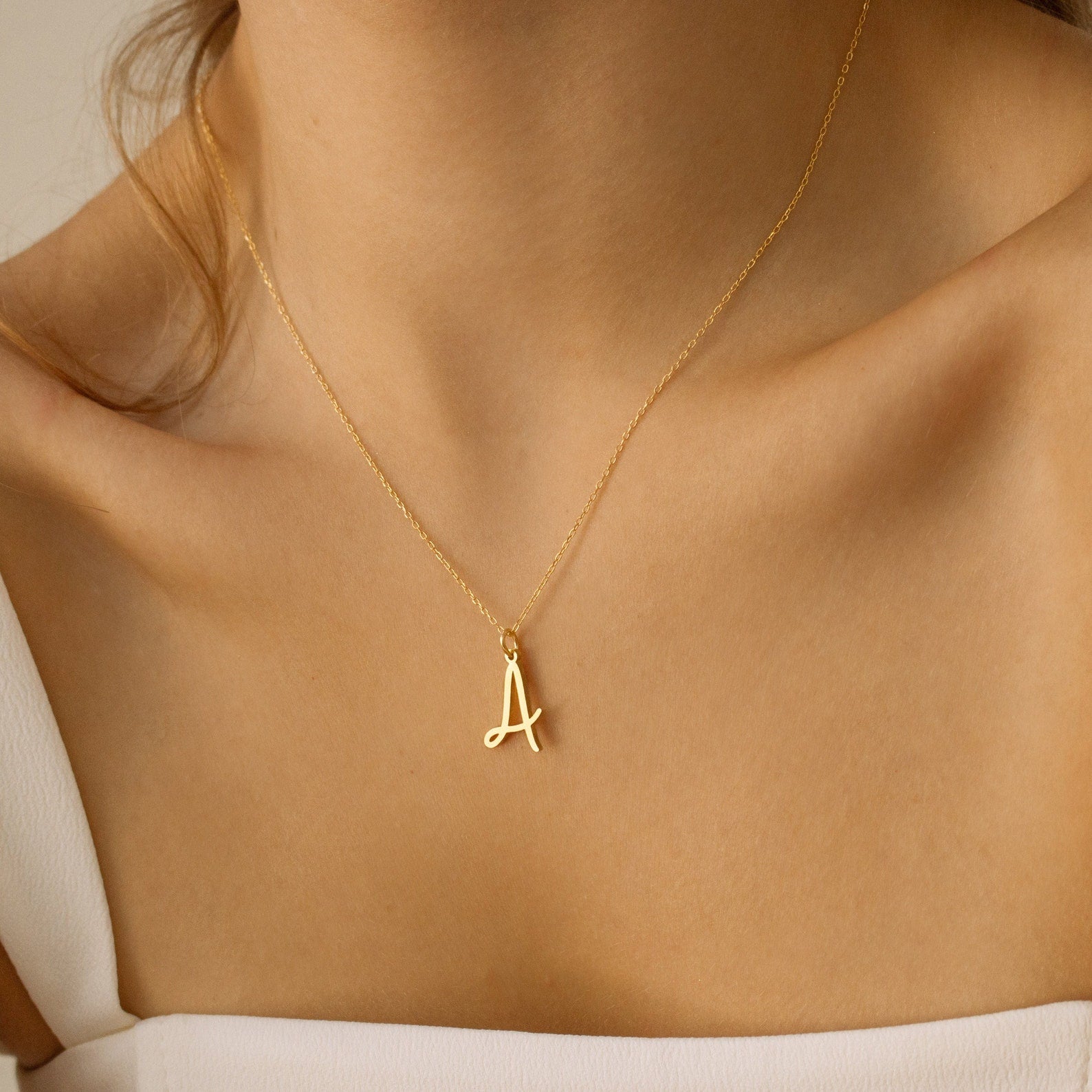 A woman wears the Nella Letter Necklace, featuring a gold pendant shaped like the letter A that elegantly rests on her neck.