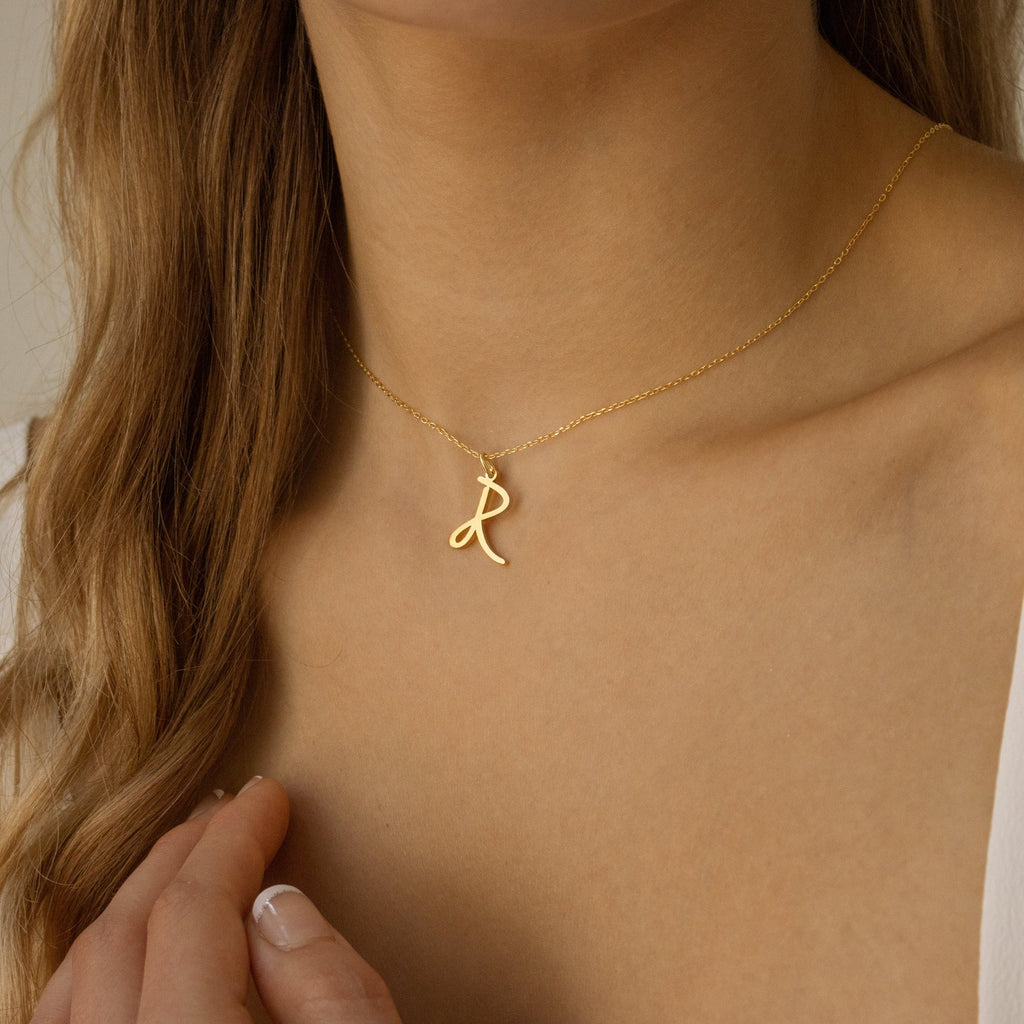 A woman wearing the Nella Letter Necklace, featuring a gold pendant with a cursive letter R.