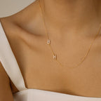 A woman wears the Pave Sideways Initial Necklace with hanging B and H charms over a white off-shoulder top.