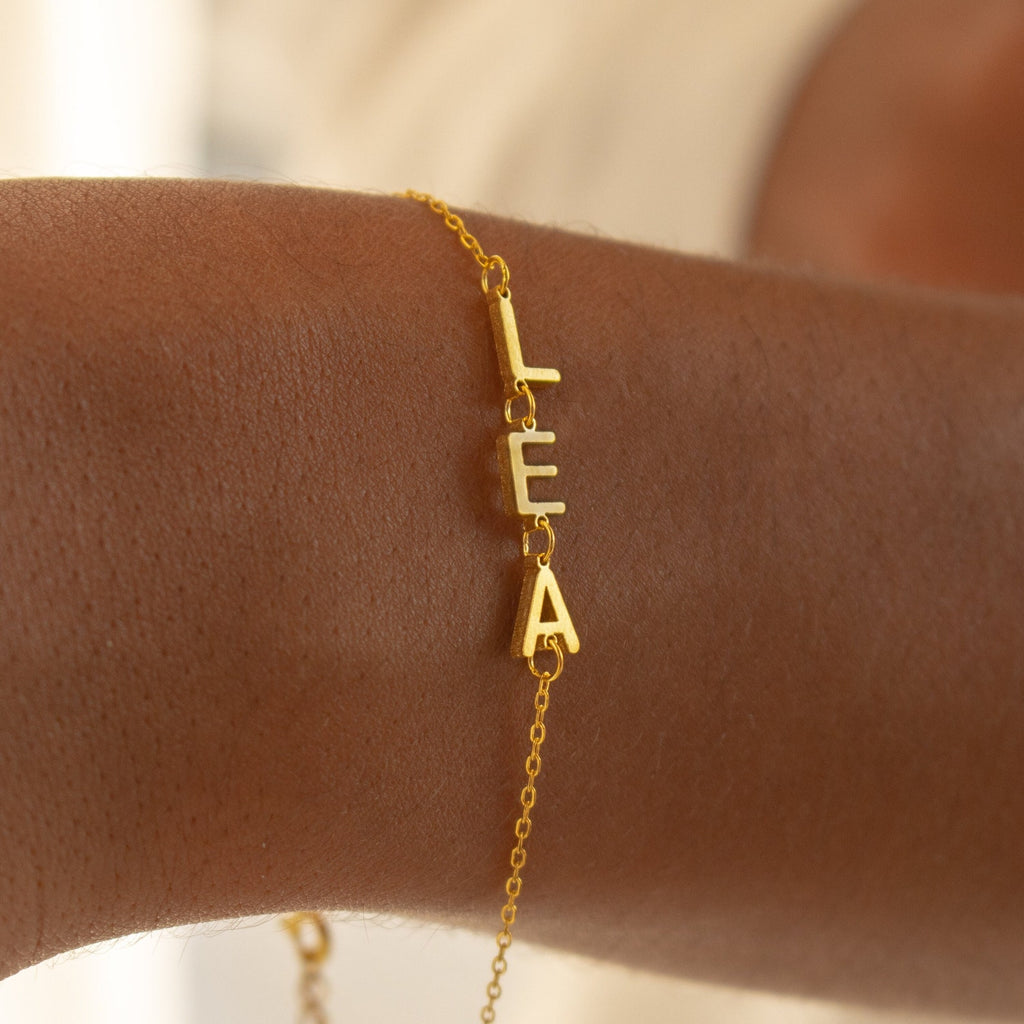 The Custom Letter Bracelet features dangling letters spelling "LEA" on the wrist—ideal for anyone who loves unique charm bracelets and personalized name jewelry.